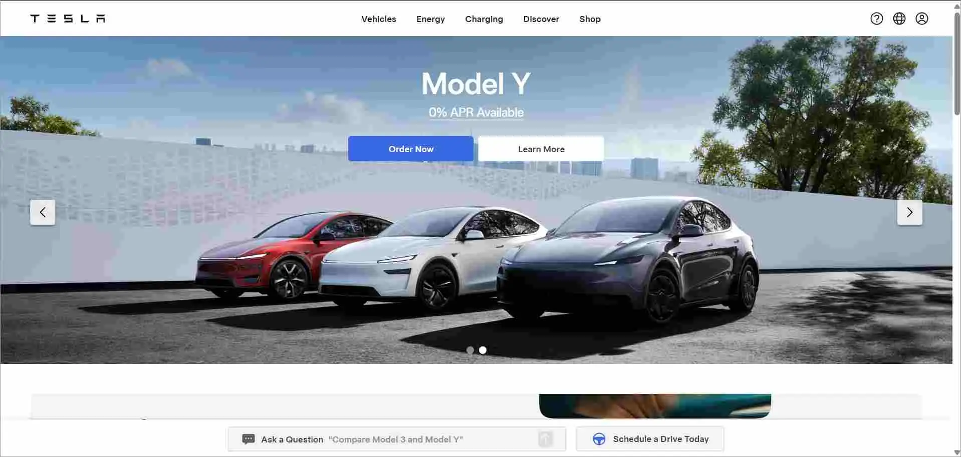 Tesla homepage with white and blue layout showing Model Y cars in red, white, and black against a clean outdoor background